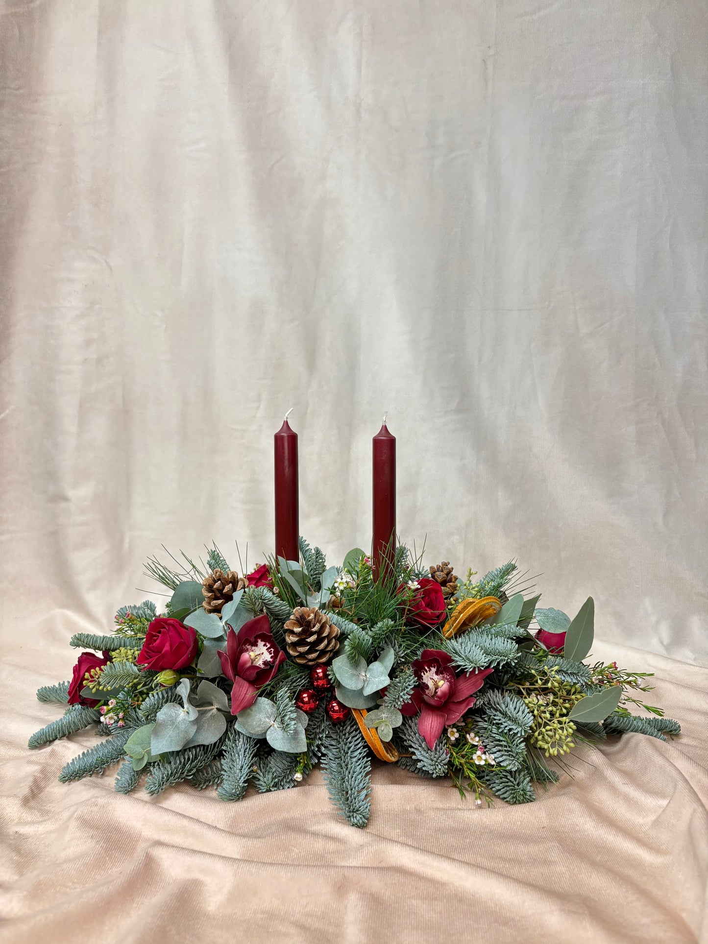Decorative Christmas floral arrangement with candles on a beige fabric background